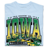 A folded heavyweight light blue t-shirt with green & gold ink that says, "Is this heaven? No, It's Iowa. Honk if you're corny" with a graphic of an old muscle car driving out of corn fields with a cat behind the steering wheel.