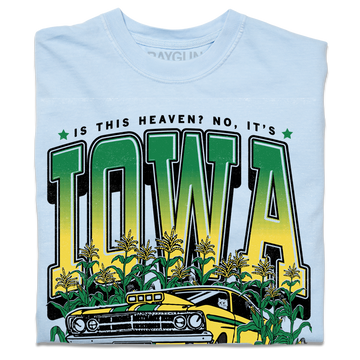 A folded heavyweight light blue t-shirt with green & gold ink that says, "Is this heaven? No, It's Iowa. Honk if you're corny" with a graphic of an old muscle car driving out of corn fields with a cat behind the steering wheel.