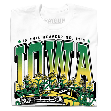 A folded white t-shirt with green & gold ink that says, "Is this heaven? No, It's Iowa. Honk if you're corny" with a graphic of an old muscle car driving out of corn fields with a cat behind the steering wheel.