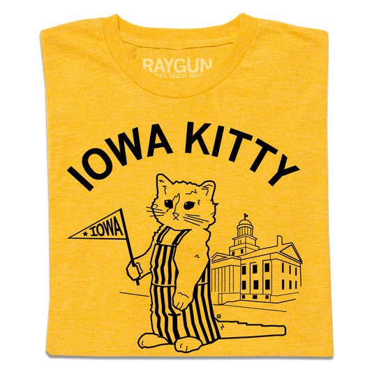 A folded heather gold shirt that says "Iowa Kitty" in black curved font over an image of RAYGUN's cat mascot, Gary, wearing striped overalls and holding a small Iowa flag in front of the old capitol building in Iowa City.
