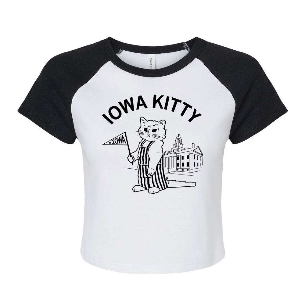 A white baby tee with black sleeves and collar that says "Iowa Kitty" in black curved font over an image of RAYGUN's cat mascot, Gary, wearing striped overalls and holding a small Iowa flag in front of the old capitol building in Iowa City.