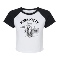 A white baby tee with black sleeves and collar that says "Iowa Kitty" in black curved font over an image of RAYGUN's cat mascot, Gary, wearing striped overalls and holding a small Iowa flag in front of the old capitol building in Iowa City.