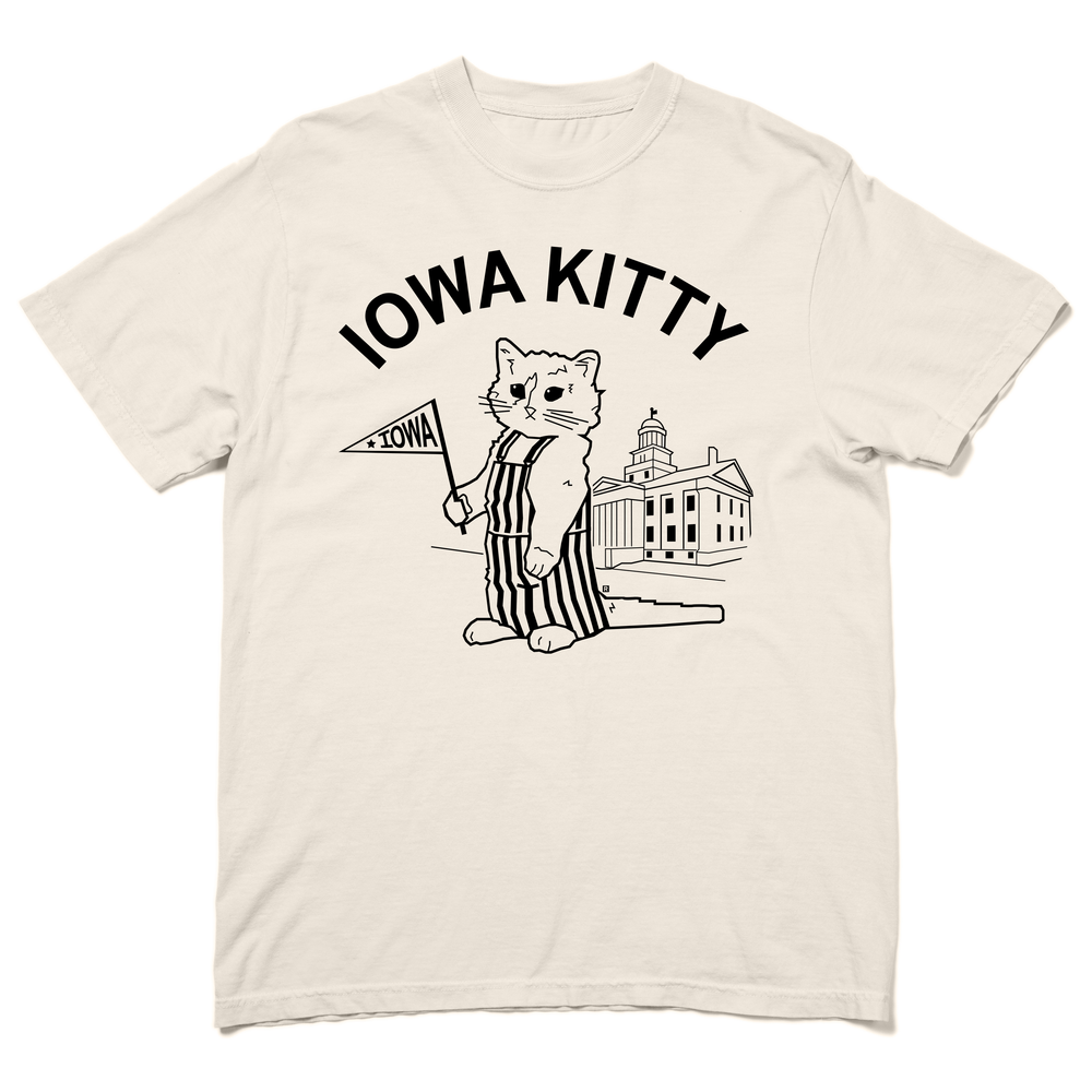 A Comfort Colors heavyweight ivory t-shirt that says "Iowa Kitty" in black curved font over an image of RAYGUN's cat mascot, Gary, wearing striped overalls and holding a small Iowa flag in front of the old capitol building in Iowa City.