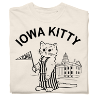 A folded heavyweight off-white t-shirt that says "Iowa Kitty" in black curved font over an image of RAYGUN's cat mascot, Gary, wearing striped overalls and holding a small Iowa flag in front of the old capitol building in Iowa City.
