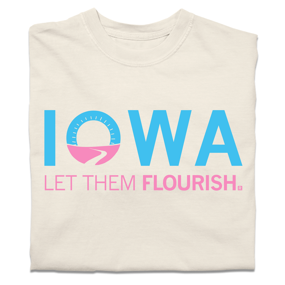 A folded ivory t-shirt with bright blue and pink print spoofing the Welcome to Iowa road signs by saying "Iowa Let Them Flourish."