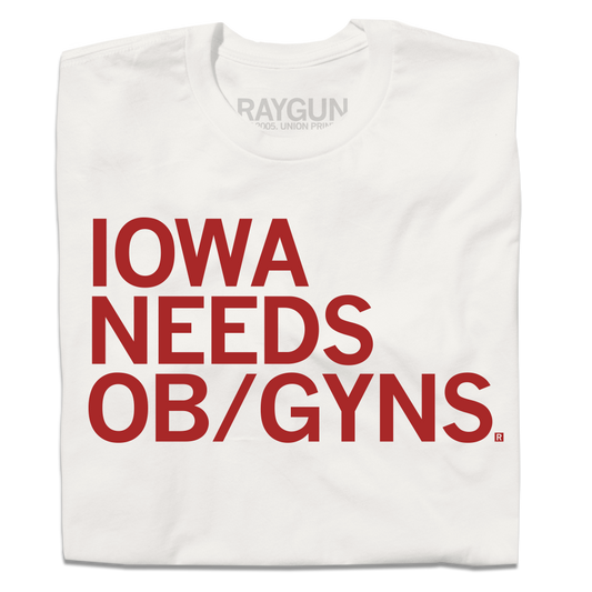 A folded off-white shirt with red left-aligned ink that reads "Iowa Needs OB/GYNs"