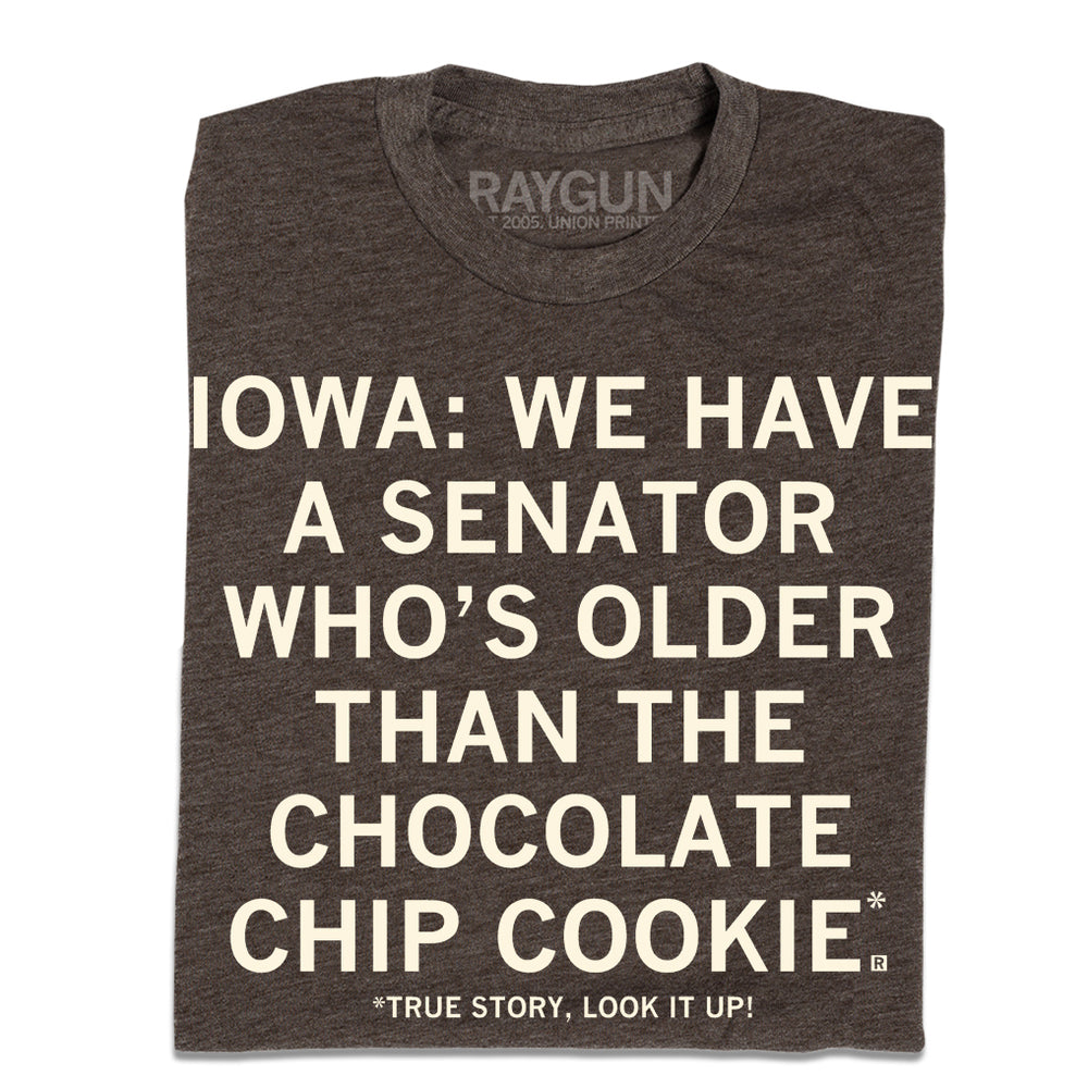 A folded heather brown t-shirt with cream ink text that reads "Iowa: We have a senator who's older than the chocolate chip cookie. True story, look it up!"