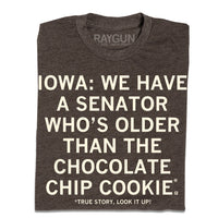 A folded heather brown t-shirt with cream ink text that reads "Iowa: We have a senator who's older than the chocolate chip cookie. True story, look it up!"