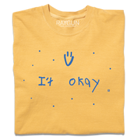 A folded heavyweight yellow t-shirt with blue print that says, "It Okay" with a smiley face above and dots scattered around. This shirt was designed by a kid taking part in a contest at our Cedar Rapids store.