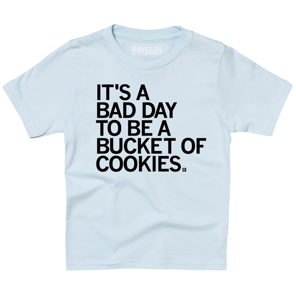 A light blue youth sized t-shirt with left aligned black text in all caps that says, "It's a bad day to be a bucket of cookies."