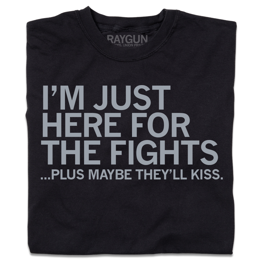 A folded black t-shirt with light grey ink that says, "I'm just here for the fights...plus maybe they'll kiss"