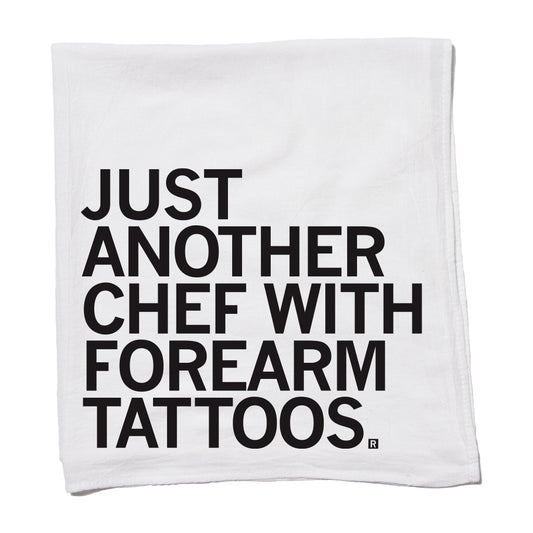 White flour sack kitchen towel printed with the black text, JUST ANOTHER CHEF WITH FOREARM TATTOOS.