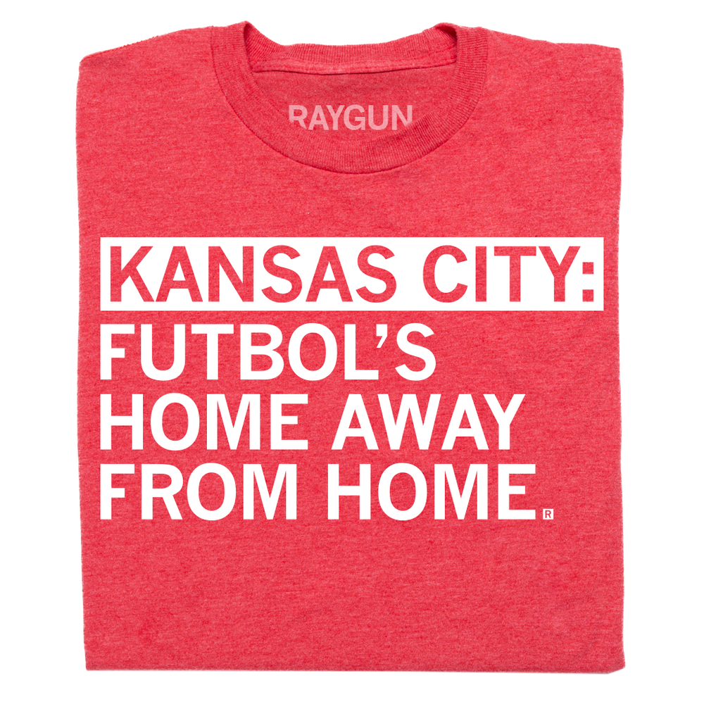 A folded heather red t-shirt with left-aligned white ink text that says, "Kansas City: Futbol's home away from home."