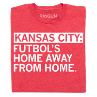 A folded heather red t-shirt with left-aligned white ink text that says, "Kansas City: Futbol's home away from home."