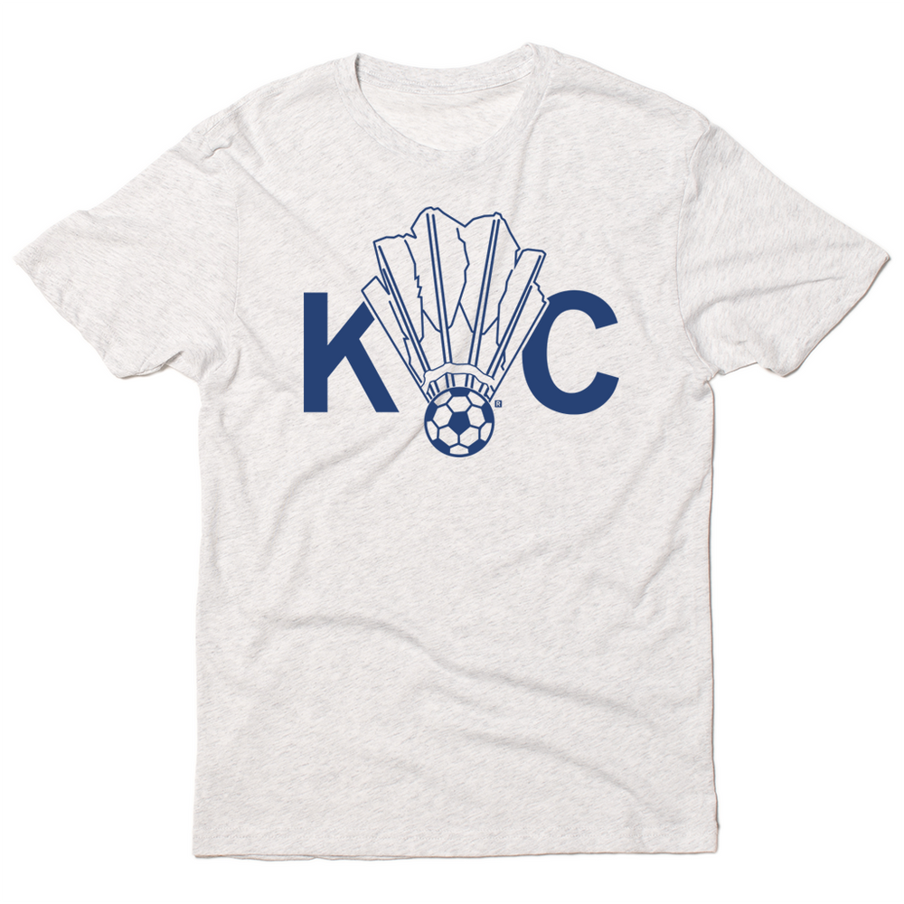Triblend heather white t-shirt with royal blue ink depicting a shuttlecock with a soccer ball at the end of it between the letters KC.