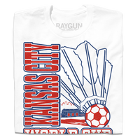 A folded white t-shirt with red & royal blue ink depicting a giant shuttlecock with a soccer ball at the end in front of an outline of the KC skyline. Text reads "World Cup Kansas City, Missouri. USA 2026."