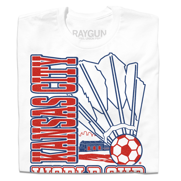 A folded white t-shirt with red & royal blue ink depicting a giant shuttlecock with a soccer ball at the end in front of an outline of the KC skyline. Text reads 