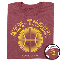 Folded heather burgundy tee with gold ink that says, "Ken-three" over a basketball on the front and "Hare 12" on the back.