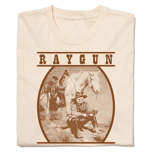 Cream-colored RAYGUN t-shirt featuring a brown graphic of a cowboy with a cat head holding a rifle next to a horse.