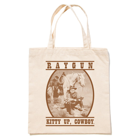 Off-white RAYGUN canvas tote bag featuring a brown graphic of a cowboy with a cat head sitting next to a horse, with the text RAYGUN above and KITTY UP, COWBOY. below.