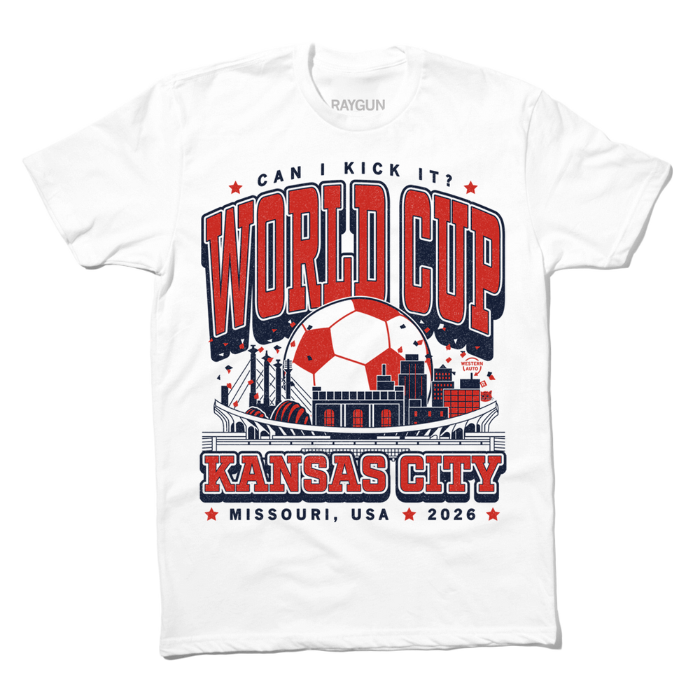 White t-shirt with red & navy ink depicting notable buildings around Kansas City behind a soccer stadium and in front of a giant soccer ball. Text reads "Can I kick it? World Cup Kansas City, Missouri. USA 2026."