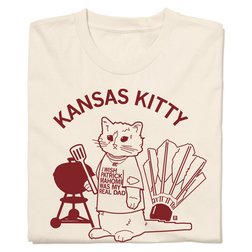 A folded off white t-shirt with an image of RAYGUN's cat mascot Garry wearing a shirt that says, "I wish Patrick Mahomes Was My Real Dad" while standing between a grill and a shuttlecock. In cardinal text above this reads "Kansas Kitty"
