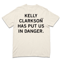 A Comfort Colors ivory heavyweight t-shirt with blank ink text that says, "Kelly Clarkson has put us in danger." with a little bird sitting on the N in "Clarkson."