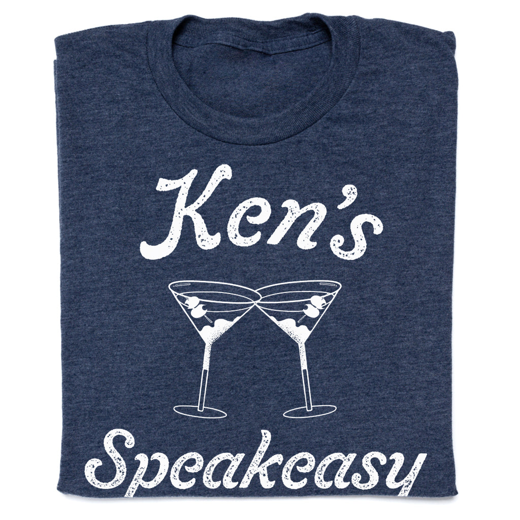 Heather denim t-shirt with white text reading Ken’s Speakeasy above an illustration of two clinking martini glasses.