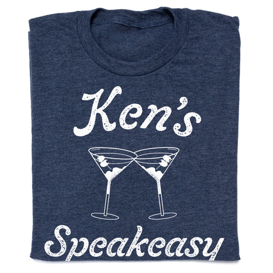 Heather denim t-shirt with white text reading Ken’s Speakeasy above an illustration of two clinking martini glasses.