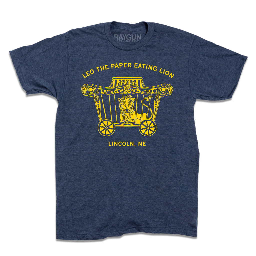 Heather denim blue t-shirt featuring a yellow graphic of a lion in a circus wagon with the text Leo the Paper-Eating Lion and Lincoln, NE.