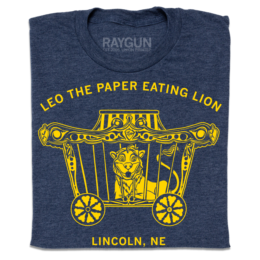 Heather denim navy blue t-shirt featuring a yellow graphic of a lion in a circus wagon with the text Leo the paper eating lion and Lincoln, NE.