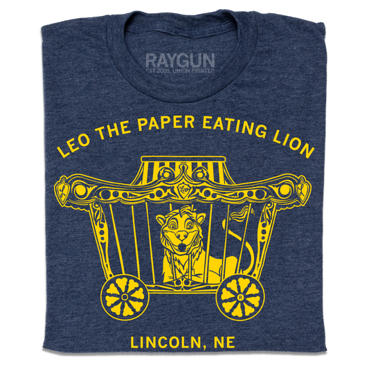 Heather denim navy blue t-shirt featuring a yellow graphic of a lion in a circus wagon with the text Leo the paper eating lion and Lincoln, NE.