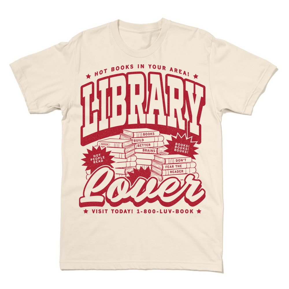 Natural t-shirt with cardinal ink. Small font across the top reads "Hot Books in your area!" then large, outlined text says, "Library Lover" with an illustration of piles of books in the center. Small text at the bottoms reads "Visit today! 1-800-luv-book"