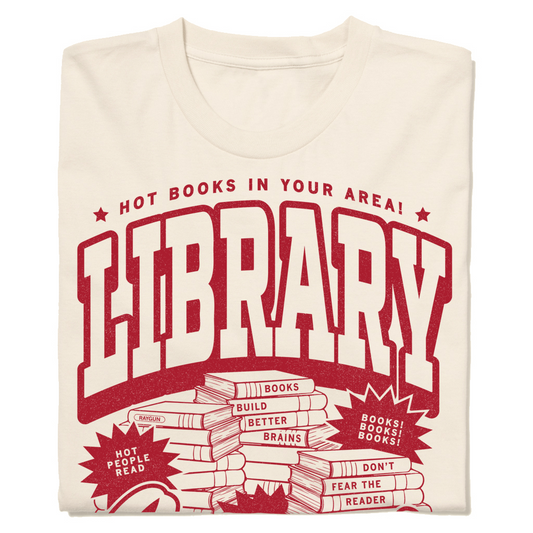 Off white t-shirt with cardinal ink. Small font across the top reads "Hot Books in your area!" then large, outlined text says, "Library Lover" with an illustration of piles of books in the center.