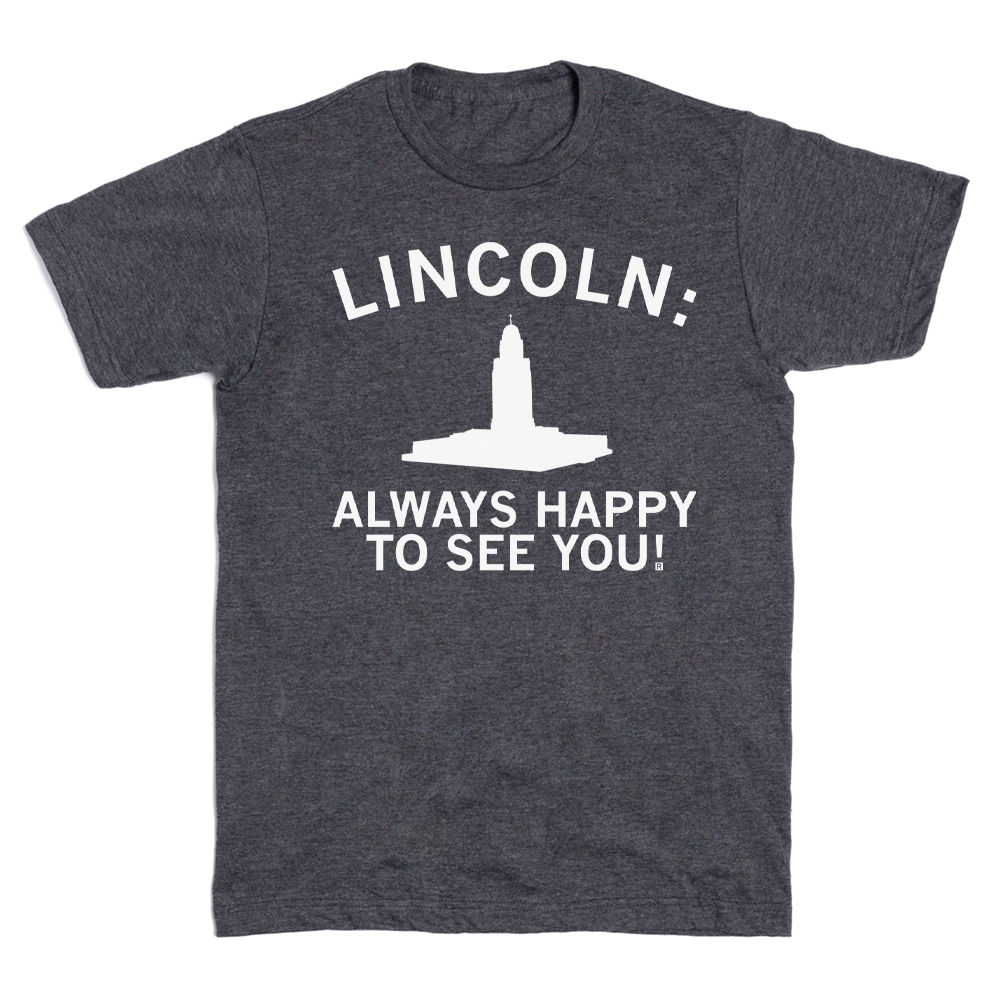 A union-made dark gray RAYGUN t-shirt featuring the text LINCOLN: ALWAYS HAPPY TO SEE YOU! above a white silhouette of the Nebraska State Capitol building.
