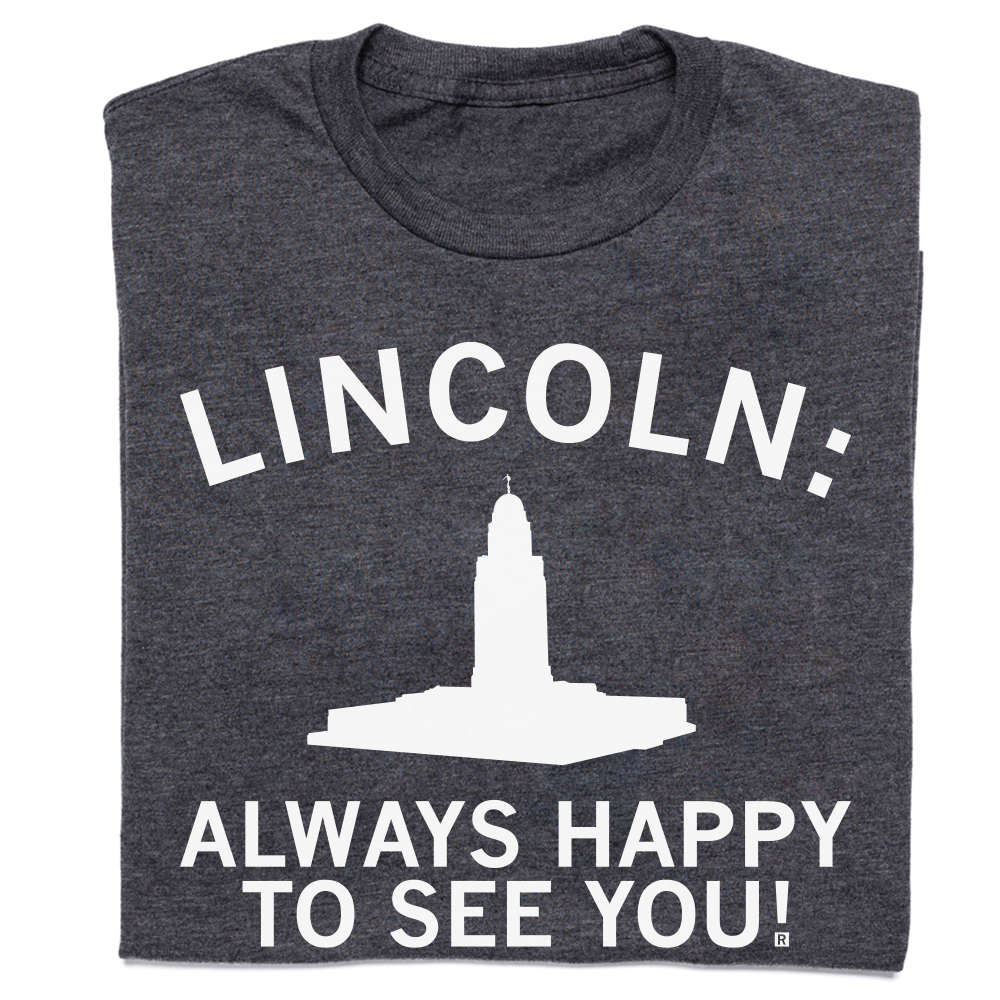 Dark gray RAYGUN crew neck t-shirt featuring the text LINCOLN: above a white silhouette of the Nebraska State Capitol building and the text ALWAYS HAPPY TO SEE YOU!.