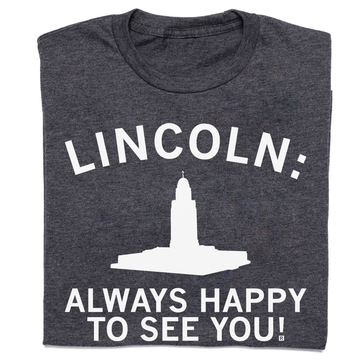 Dark gray RAYGUN crew neck t-shirt featuring the text LINCOLN: above a white silhouette of the Nebraska State Capitol building and the text ALWAYS HAPPY TO SEE YOU!.