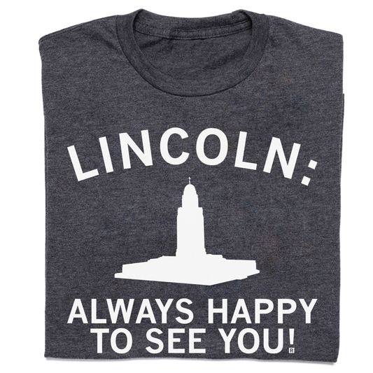 Dark gray RAYGUN crew neck t-shirt featuring the text LINCOLN: above a white silhouette of the Nebraska State Capitol building and the text ALWAYS HAPPY TO SEE YOU!.