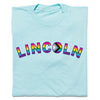 Light blue RAYGUN t-shirt featuring the word LINCOLN in rainbow-colored letters, with the letter O designed as a Progress Pride flag for Lincoln NE Pride.