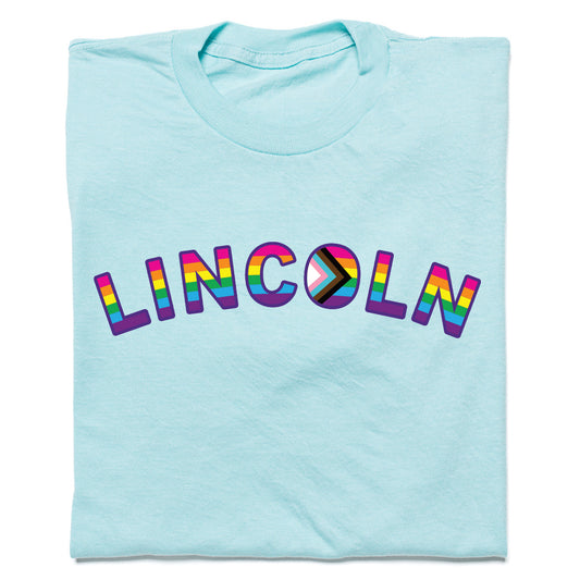Light blue RAYGUN t-shirt featuring the word LINCOLN in rainbow-colored letters, with the letter O designed as a Progress Pride flag for Lincoln NE Pride.