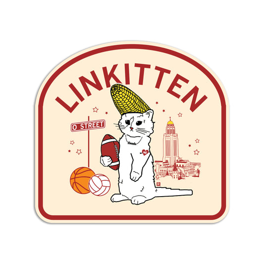 A RAYGUN vinyl sticker featuring a cat wearing a corn cob hat, holding a football beside a basketball and volleyball. The design includes LINKITTEN text, a street sign, and the Nebraska State Capitol in the background.