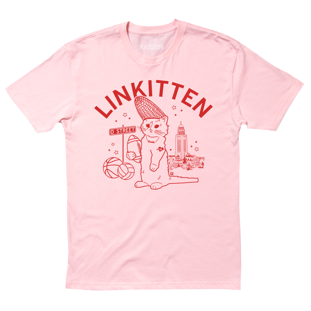 A pink tee with red ink that says "Linkitten" in curved font above RAYGUN's cat mascot wearing a corn cobb hat and holding a football. Behind him are Lincoln landmarks, like the NE state Capitol.