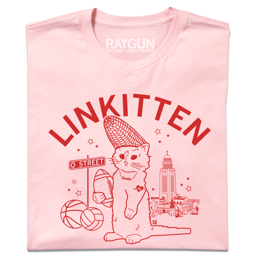 Folded light pink t-shirt with bright red ink that says "Linkitten" in curved font above RAYGUN's cat mascot wearing a corn cobb hat and holding a football. Behind him are Lincoln landmarks, like the NE state Capitol.