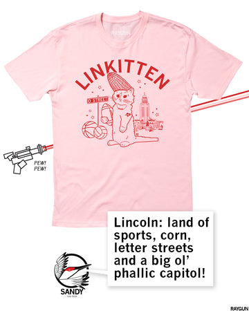 Pink t-shirt with a red graphic of a cat wearing a corn cob hat, holding a football, near a street sign labeled O Street, a basketball, and a capitol building, with the text LINKITTEN above and a speech bubble describing Lincoln, Nebraska.