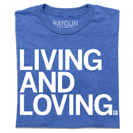 A folded heather royal blue t-shirt with large, left-aligned white ink text that reads "Living and Loving"