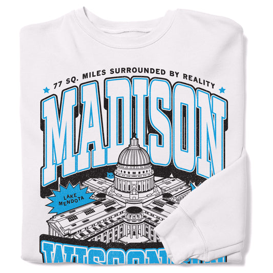White sweatshirt featuring a graphic of the Wisconsin State Capitol, the text MADISON, and the phrase 77 SQ. MILES SURROUNDED BY REALITY, designed and printed in the USA.