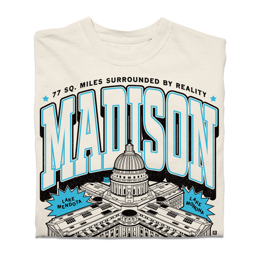 Cream-colored heavyweight Madison, WI t-shirt featuring a graphic of the State Capitol, the text MADISON, 77 SQ. MILES SURROUNDED BY REALITY, and labels for Lake Mendota and Lake Monona.
