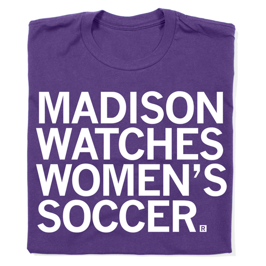 A folded purple t-shirt with left aligned text in white ink that reads "Madison watches women's soccer"