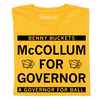 A folded heather gold shirt with black ink text that reads "Benny Buckets. McCollum for Governor. A Governor for ball."