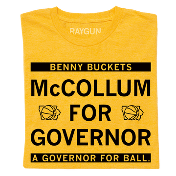 A folded heather gold shirt with black ink text that reads "Benny Buckets. McCollum for Governor. A Governor for ball."
